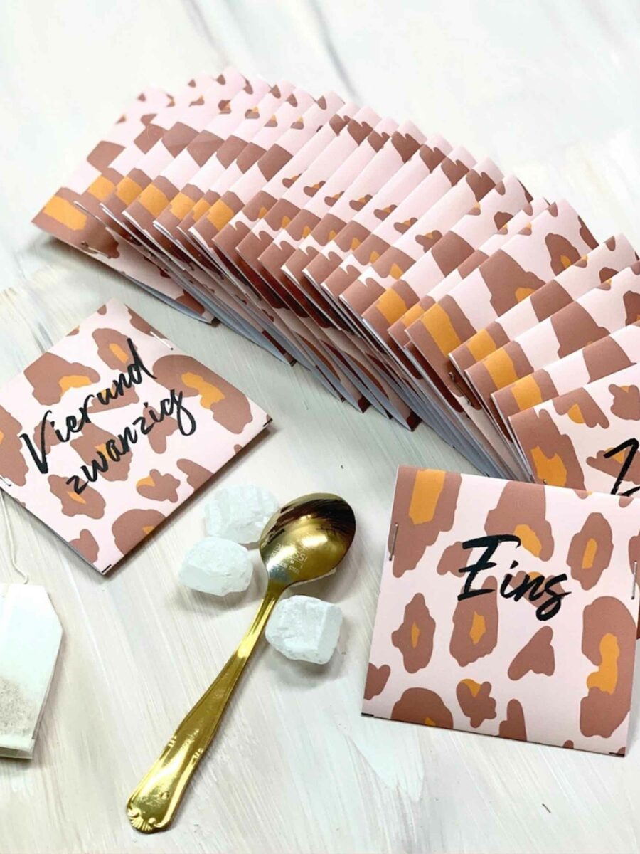 Ein Adventskalender-Set von Anke mit nummerierten Tütchen im Leopardenmuster, ergänzt durch einen goldenen Löffel und Zuckerstücke auf hellem Untergrund.