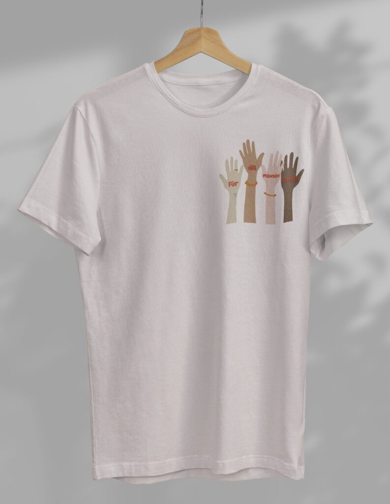 Weißes T-Shirt auf einem Holzkleiderbügel mit einer Illustration von vier verschiedenfarbigen Händen und dem Schriftzug Für die Menschlichkeit.