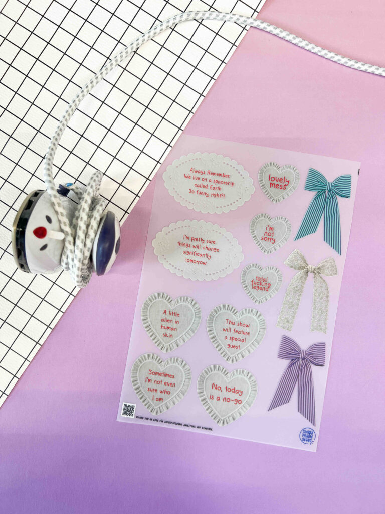 Ein Stickerbogen von Anke mit herzförmigen Sprüchen und Schleifen-Illustrationen auf einem Hintergrund mit Gittermuster und einem Kabel.