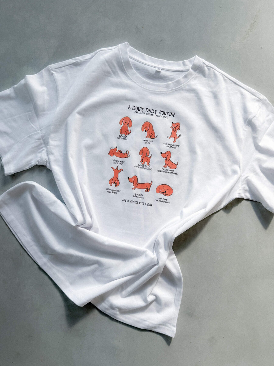 Weißes T-Shirt mit einer Illustration von Anke, die den Tagesablauf eines Hundes mit acht kleinen, niedlichen Dackel-Zeichnungen humorvoll darstellt.