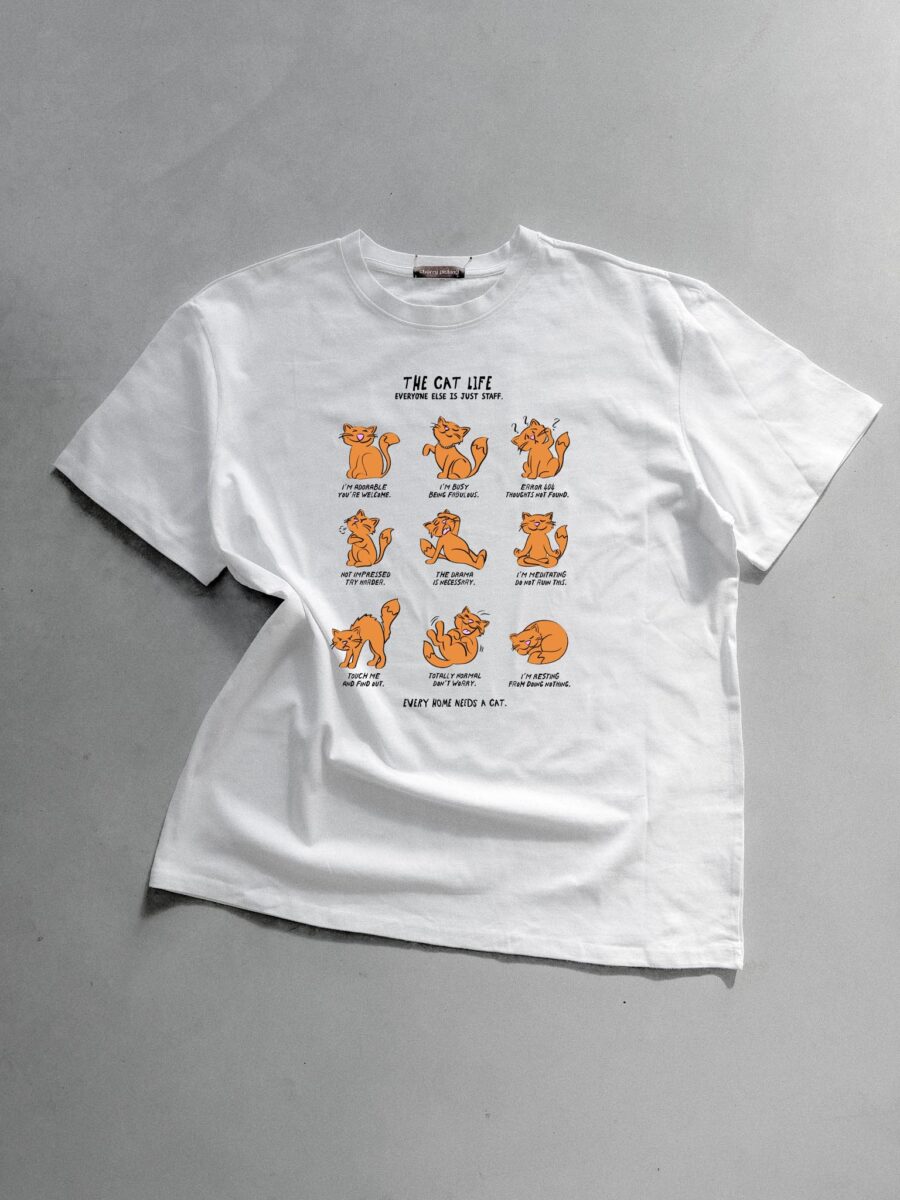 Weißes T-Shirt mit einer Illustration von neun verschiedenen orangefarbenen Katzen, die humorvoll den Alltag und das Leben mit Katzen darstellen.