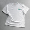Weißes T-Shirt von Cherry Picking mit einem kleinen, aufgestickten Dackel im grün-weißen Karomuster auf der Brust vor einem hellgrauen Hintergrund.