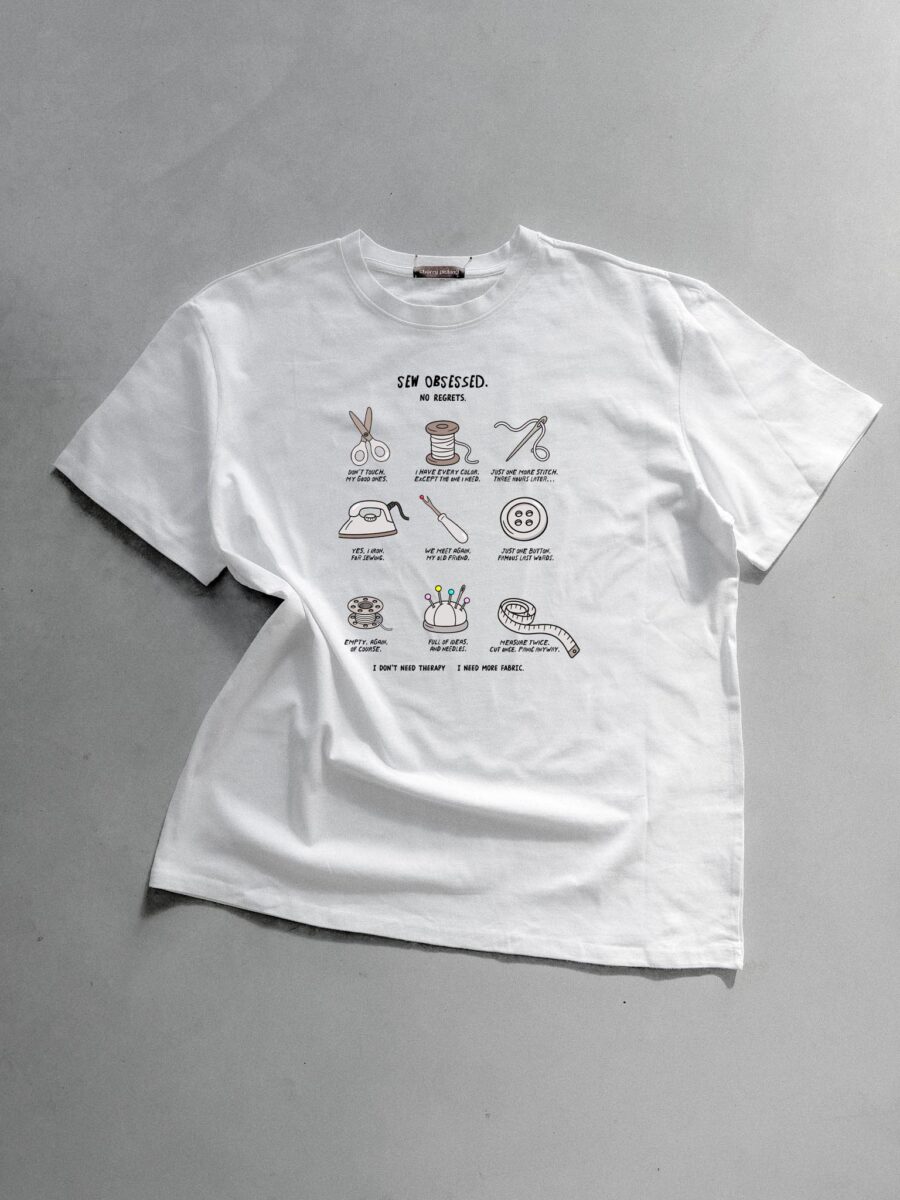 Weißes T-Shirt mit einer Illustration von Nähutensilien und dem Schriftzug Sew Obsessed, entworfen von der Künstlerin Anke für Cherry Picking.