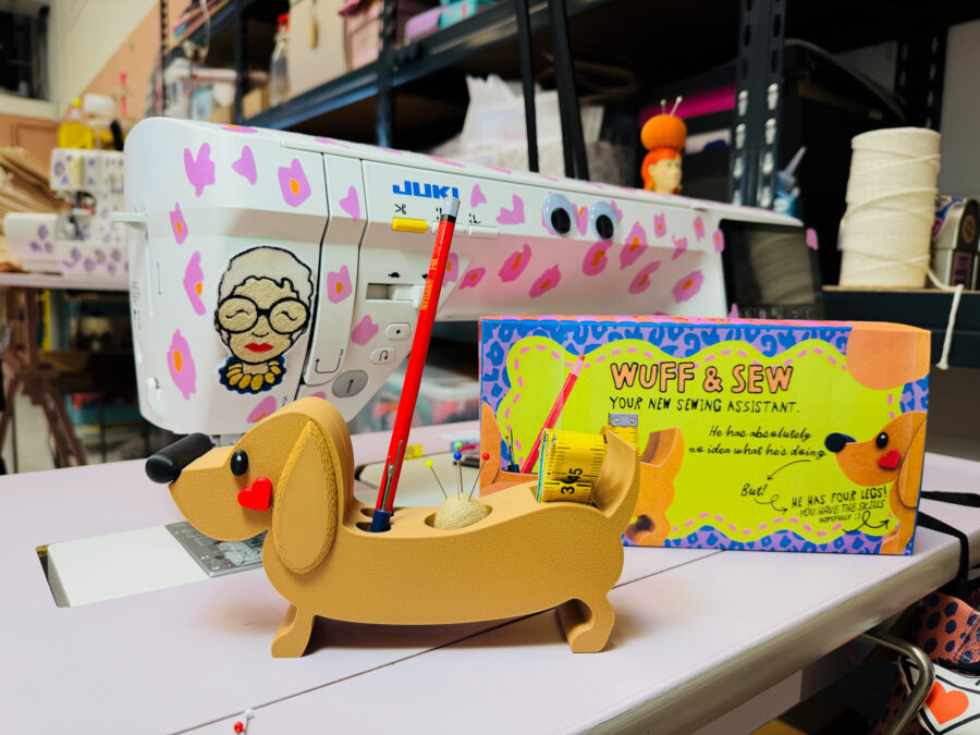 Ein beiger Dackel-Nadelkissenhalter vor einer Juki-Nähmaschine und der Wuff & Sew-Produktverpackung in einem kreativen Atelier von Künstlerin Anke.
